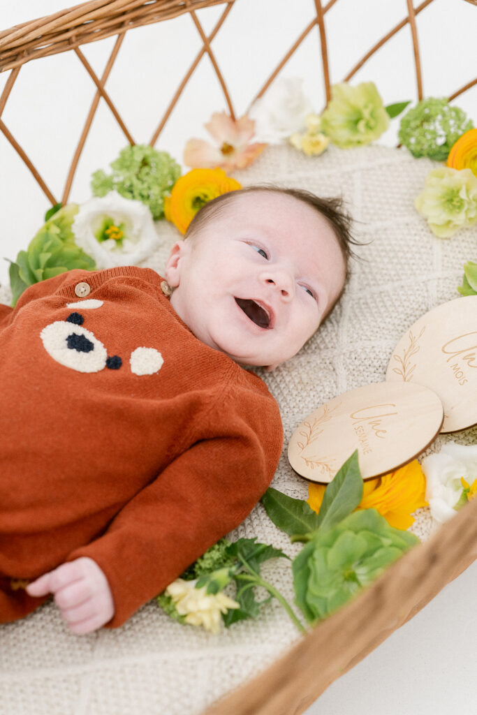 Photographe naissance Reims – bébé Raphaël souriant dans un panier fleuri au studio
